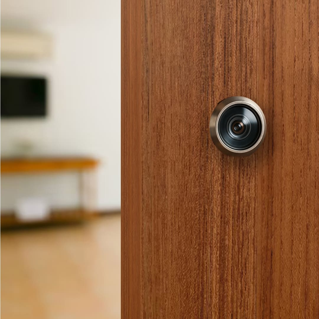 Mirilla metálica en primer plano instalada en una puerta de madera, con su canto e interior del hogar visibles